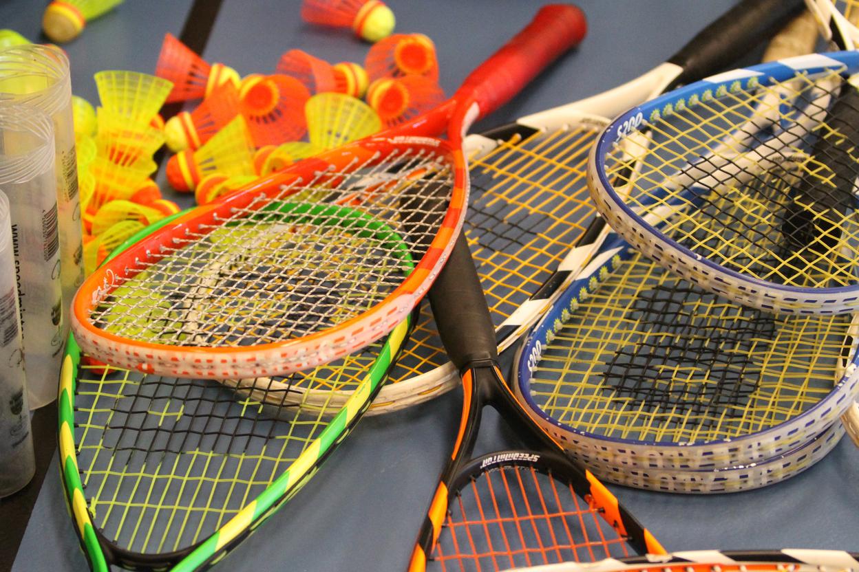 Bunte Badminton-Schläger und -Bälle liegen auf einem Tisch, umgeben von transparenten Schutzhüllen.