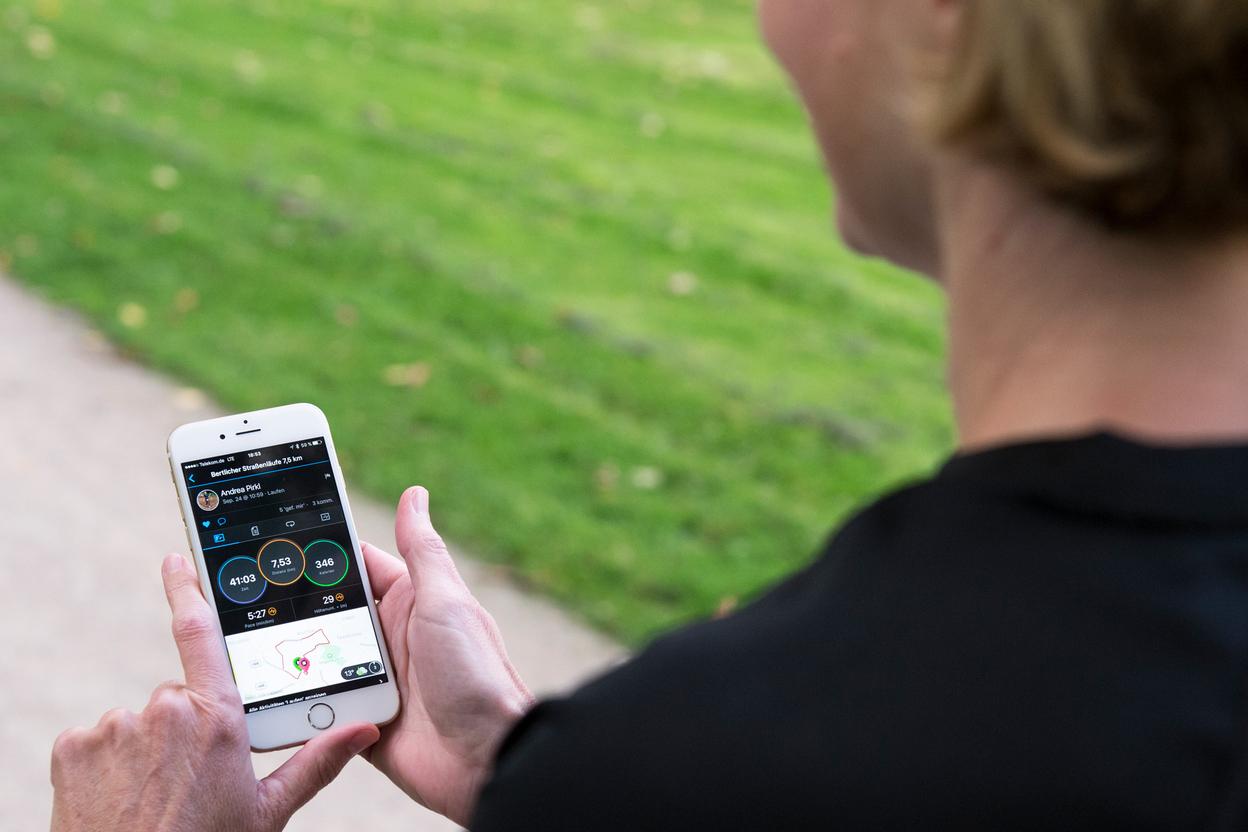 Person hält ein Smartphone mit Laufstatistiken in der Hand, während sie auf einem Weg im Freien steht.