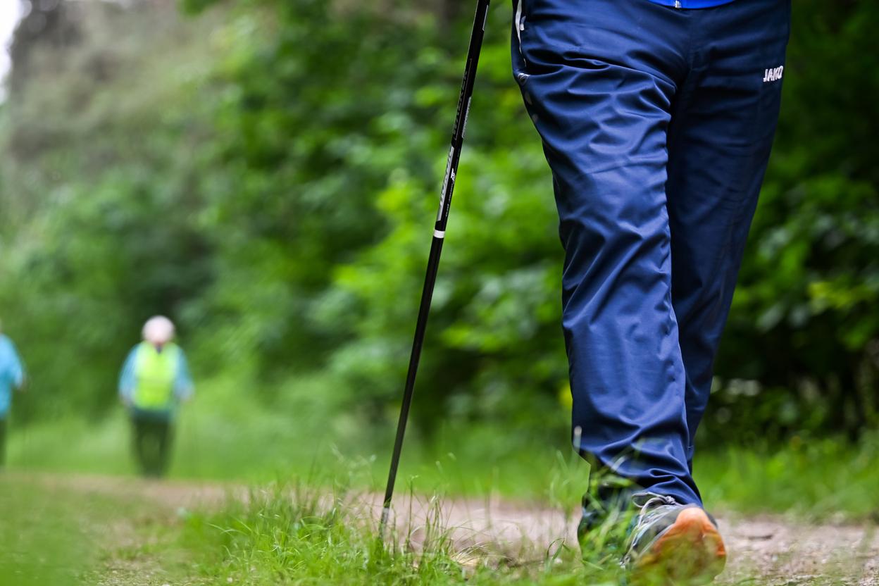 Nahaufnahme eines wandernden Fußes mit Trekkingstock auf einem schmalen Weg, im Hintergrund zwei weitere Personen.