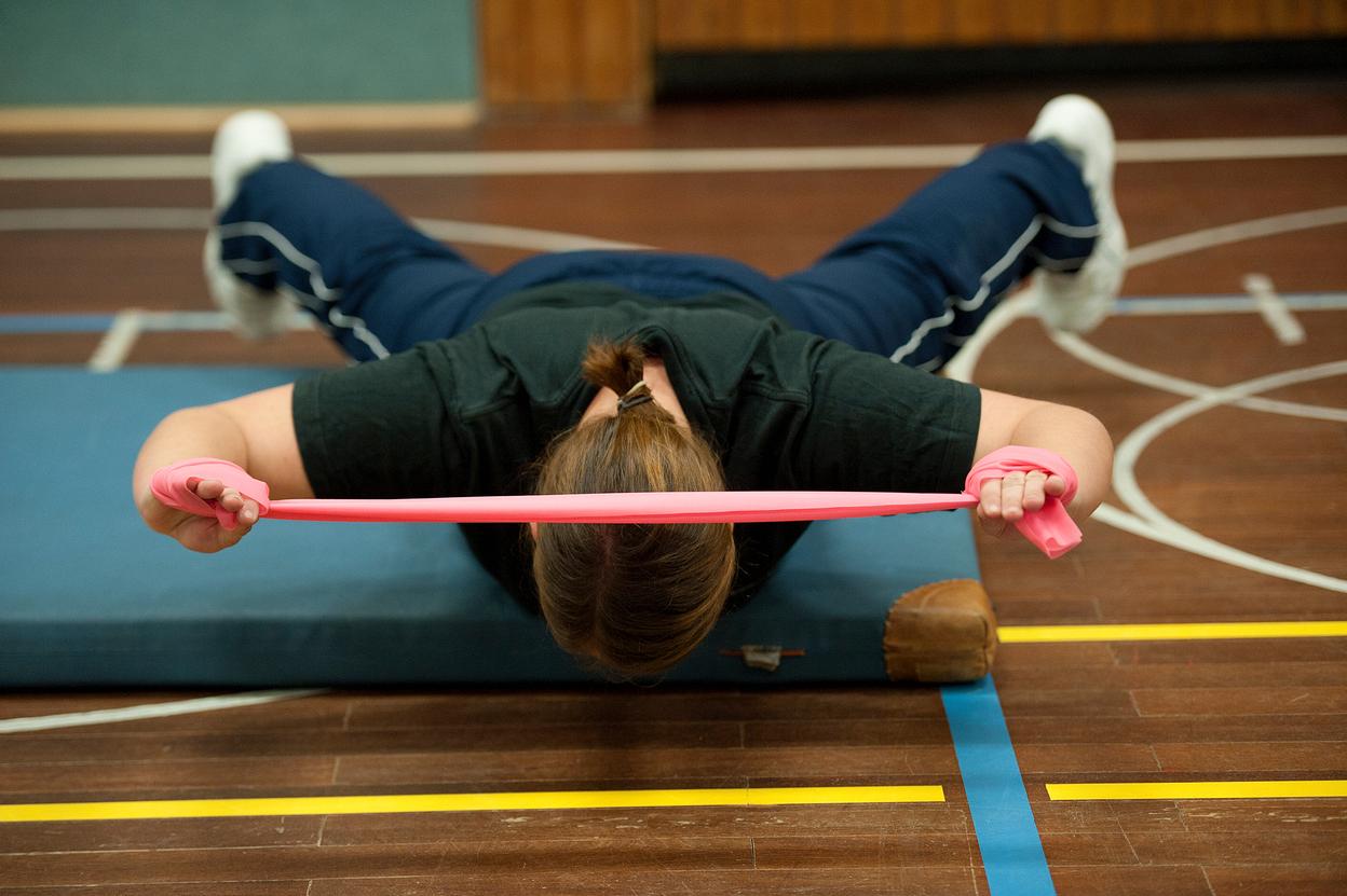 Frau führt eine Übung mit einem pinken Widerstandsband auf einer Matte in einem Sportbereich aus.