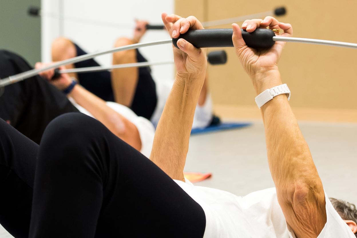 Ältere Personen machen auf Gymnastikmatten Liegestütze mit Widerstandsband in einem Trainingsraum.